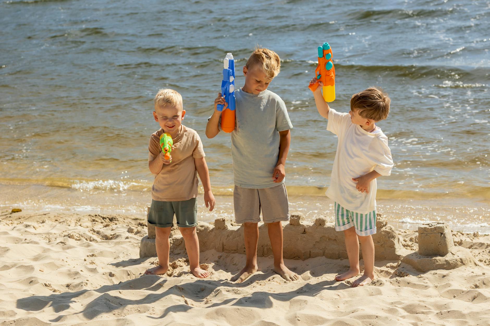 Chłopcy bawią się pistoletami wodnymi na piaszczystej plaży latem