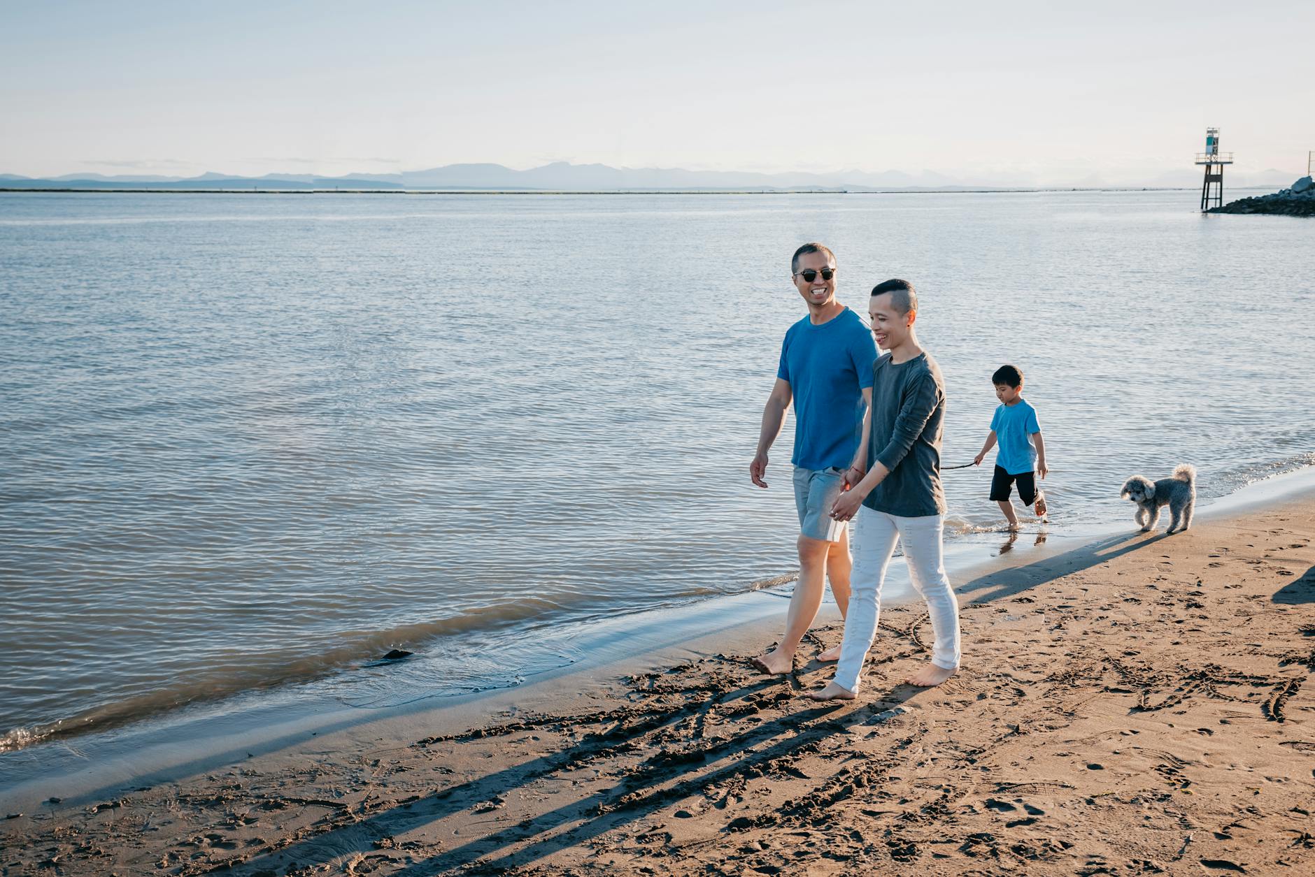 Dwóch ojców z dzieckiem i psem spacerują po spokojnej plaży nad morzem