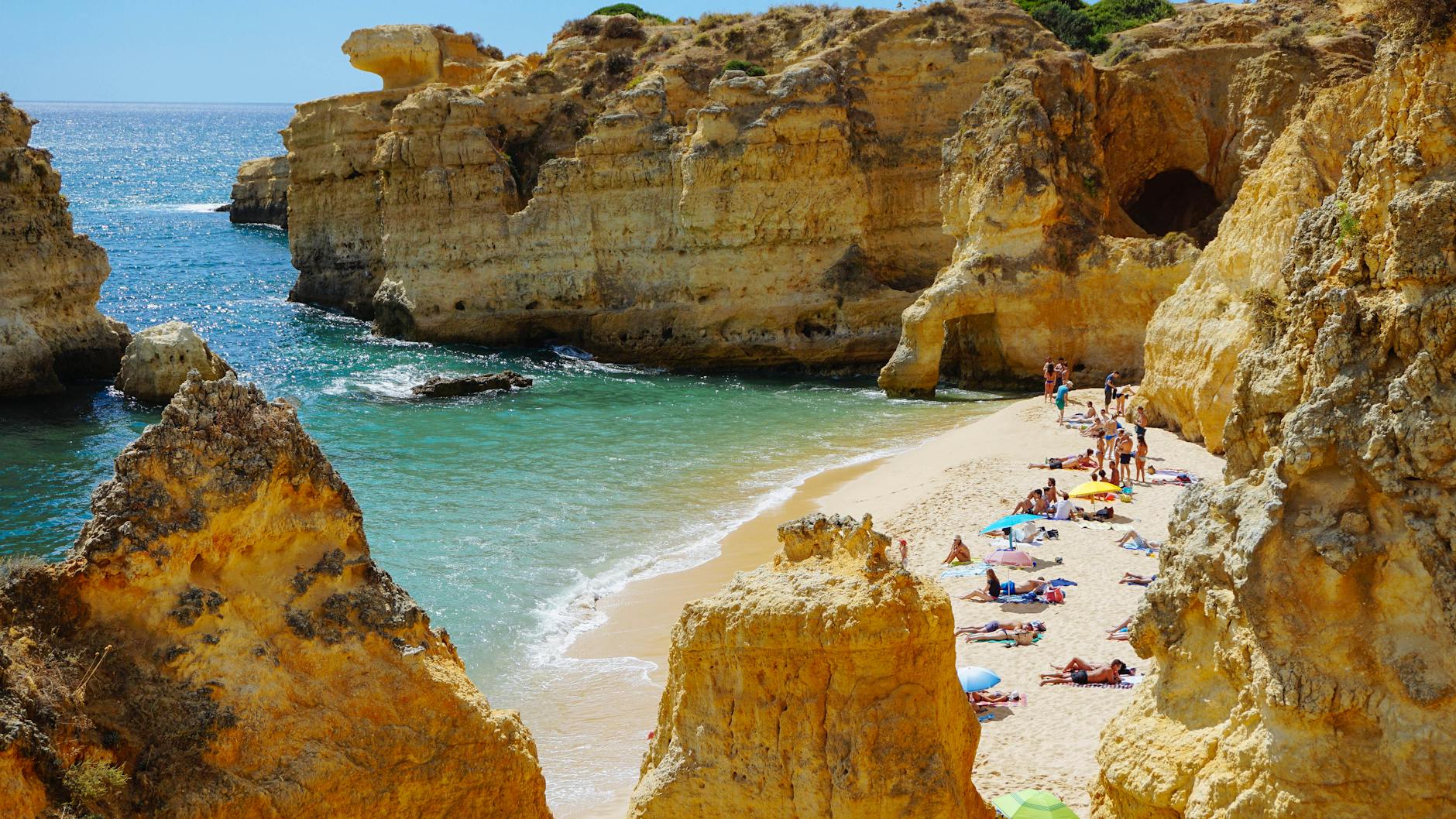 Najlepsze europejskie plaże na czerwcowe urlopy, zanim zacznie się wysoki sezon Plaża w Algarve z klifami, turkusowym morzem i opalającymi się turystami