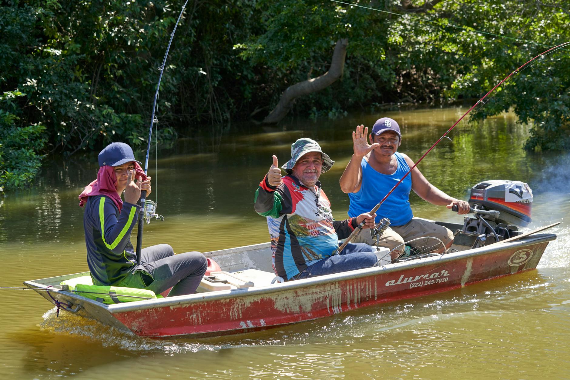 Trzech wędkarzy łowi z łodzi na słonecznej rzece
