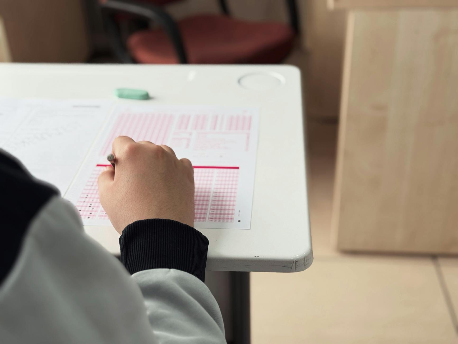 Uczeń w sali egzaminacyjnej wypełnia test na kartce