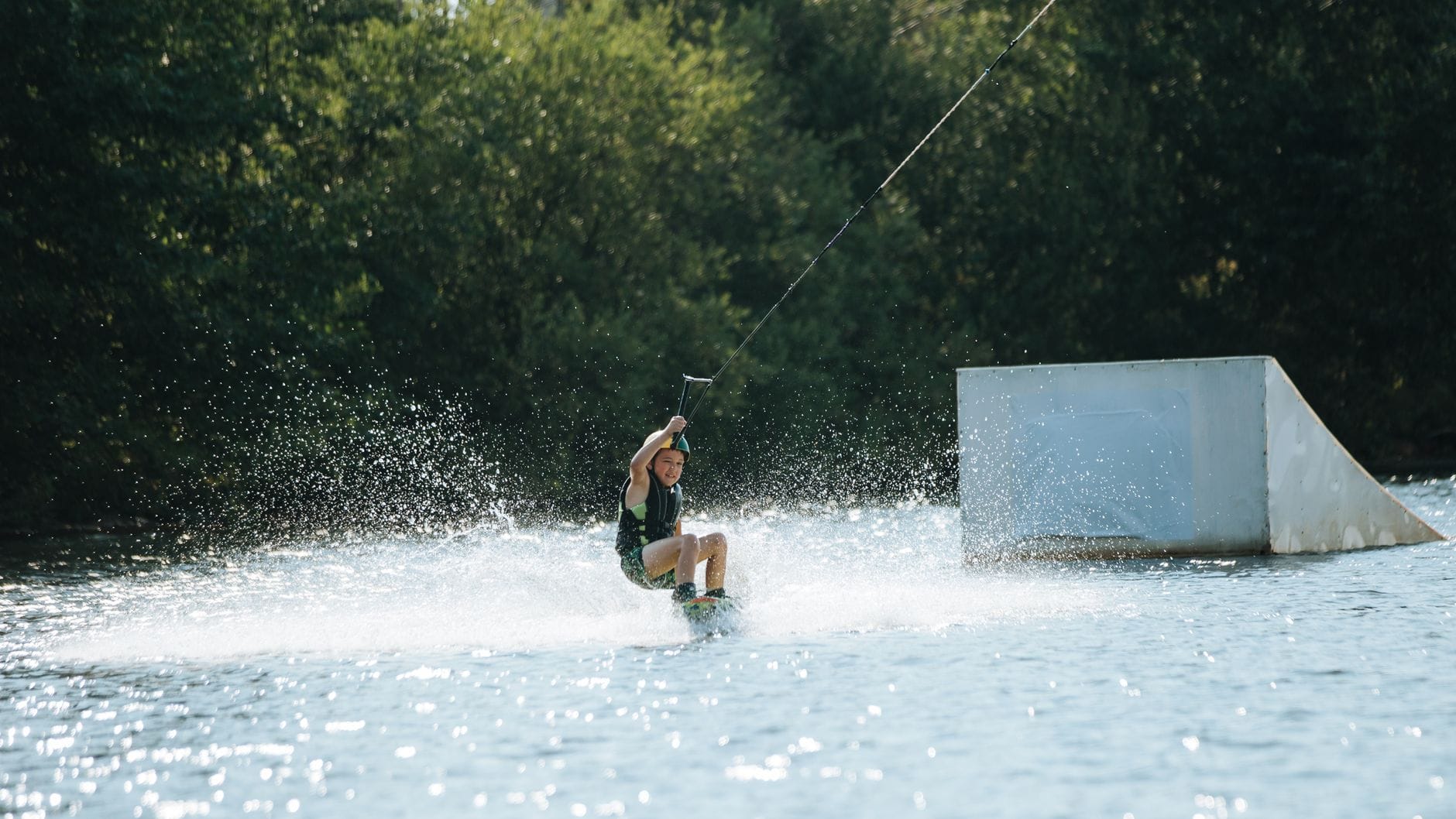Aquaparki pod chmurką w Polsce gdzie połączyć baseny z plażowaniem nad jeziorem Dziecko na wakeboardzie na jeziorze w letnim aquaparku na świeżym powietrzu
