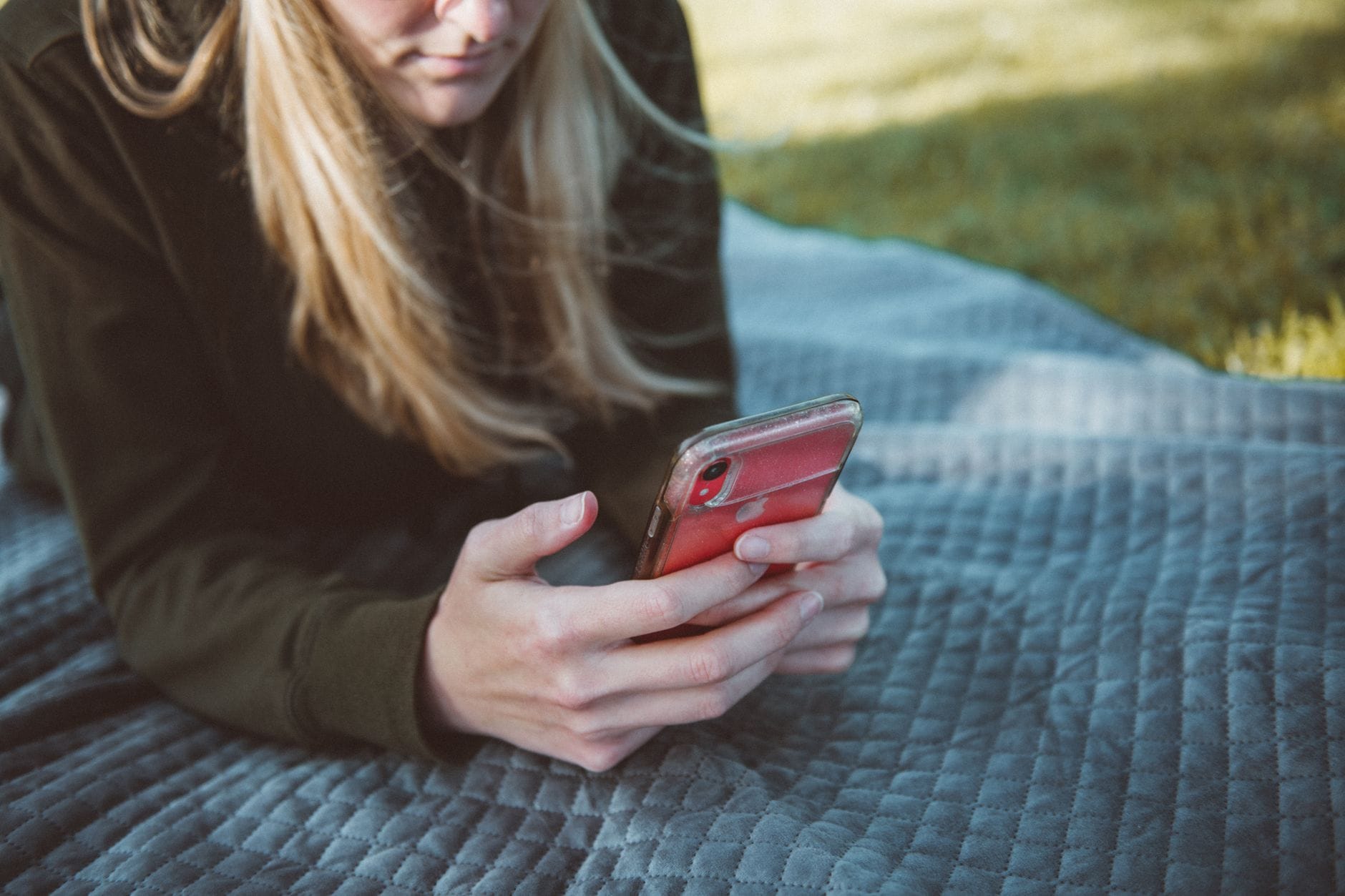 Młoda kobieta na kocu używa smartfona do obserwacji przyrody