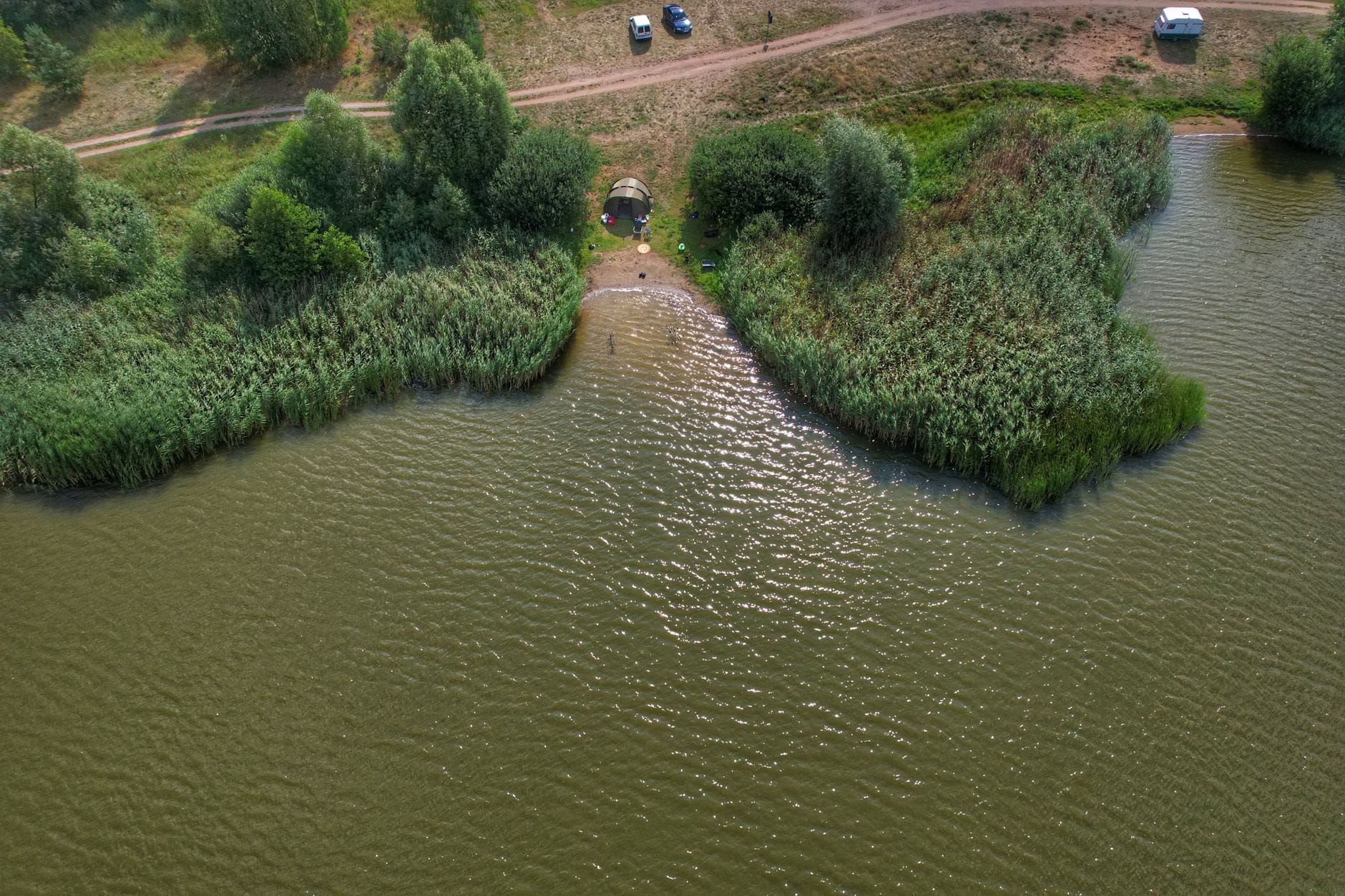 Namiot nad spokojnym jeziorem otoczonym zielenią z lotu ptaka