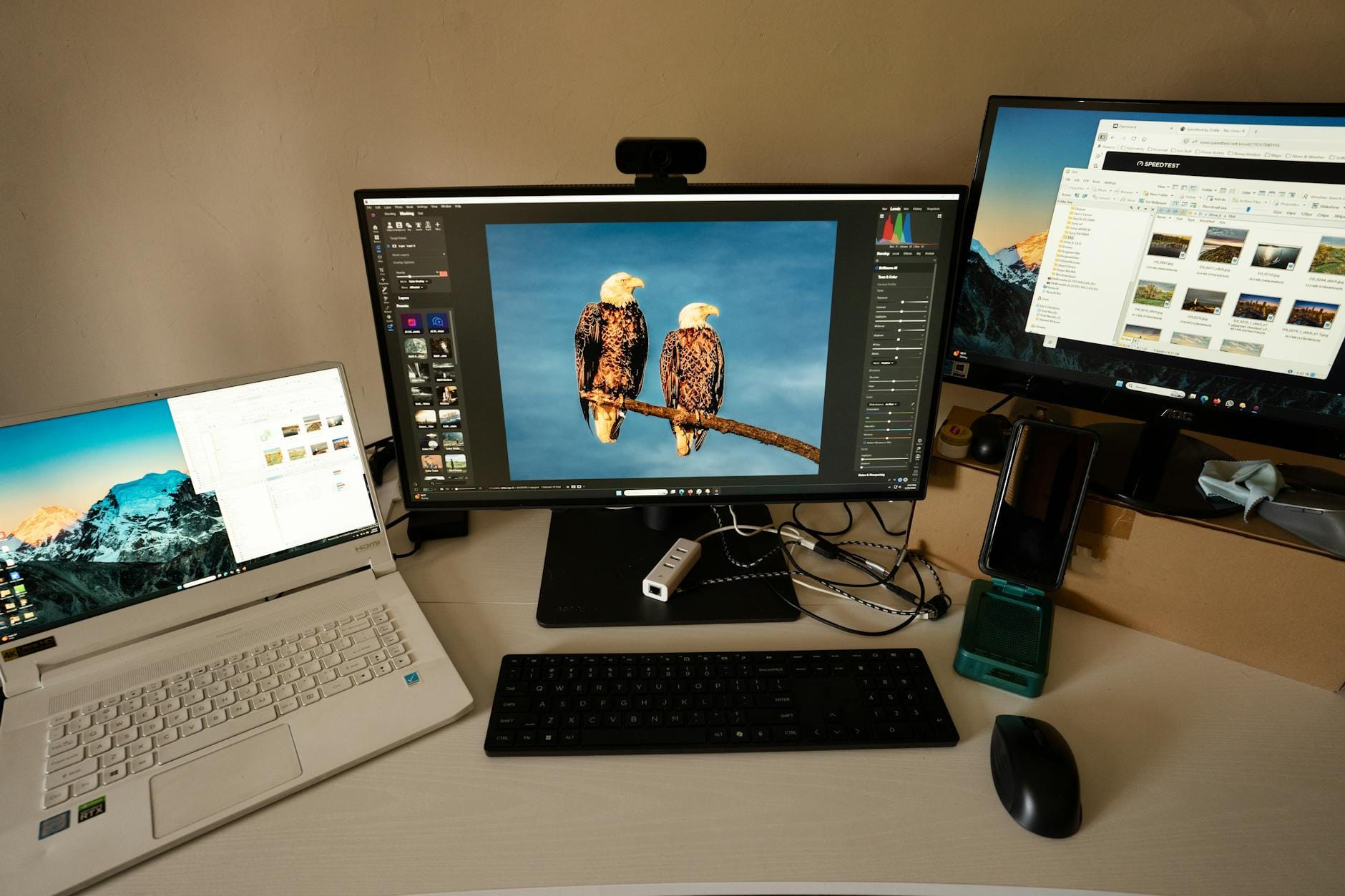Stanowisko pracy fotografa z dwoma monitorami, laptopem i edytorem zdjęć